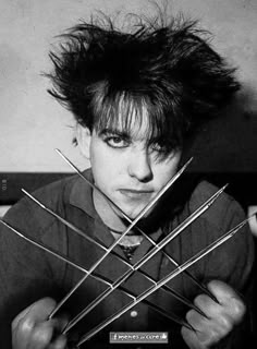 a young man holding up six pairs of needles in front of his face and looking at the camera