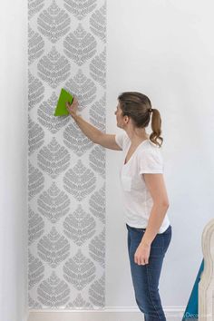 a woman is using a green brush to paint a wallpaper pattern on the wall