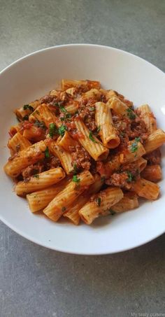 a white bowl filled with pasta covered in sauce and parsley on top of a table