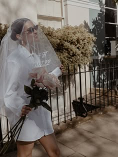 a woman is walking down the street with a veil on her head and flowers in her hand