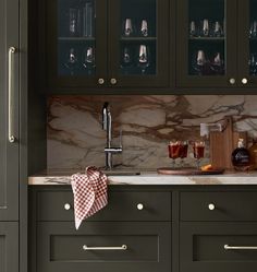 a kitchen with green cabinets and marble counter tops, wine glasses on the cabinet doors