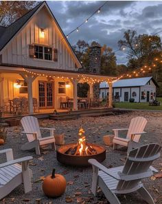 an outdoor fire pit with chairs around it and lights strung over the front of the house