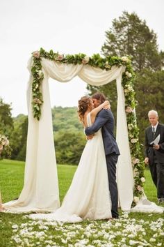 a bride and groom kissing under an outdoor wedding ceremony chute with white flowers on the grass