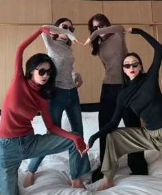 four women are jumping on a bed with their arms in the air while wearing sunglasses