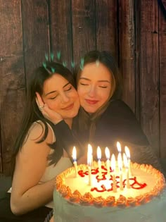 two women hugging each other in front of a birthday cake with lit candles on it