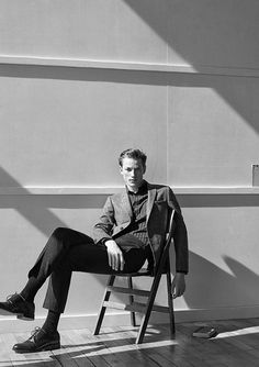 a man sitting on a chair in front of a wall with his legs crossed and feet crossed