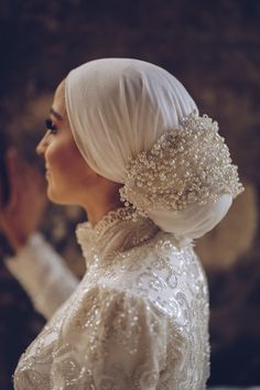 a woman in a white dress with pearls on her head and hands behind her back