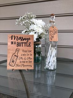 a message in a bottle is placed on a table next to a vase with flowers