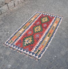 a multicolored rug on the ground in front of a stone wall and cobblestone walkway