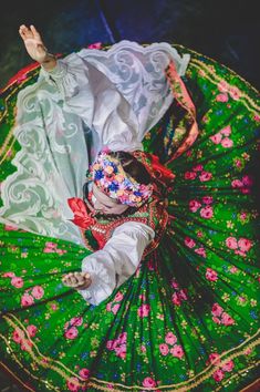 a woman is laying on the ground in a colorful dress and headdress, with her arms outstretched