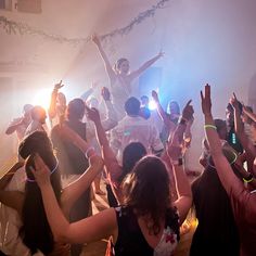 a group of people standing around each other in a room with their arms raised up