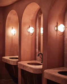 a row of sinks in a bathroom with arched walls and lights on the wall above them