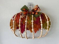 a white pumpkin shaped wall hanging with wooden beads and bows on it's side