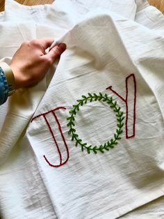 someone's hand is stitching the word joy on a white towel with red thread