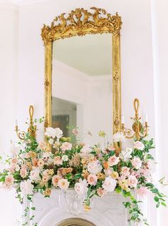 a fireplace decorated with flowers and greenery in front of a large mirror above it