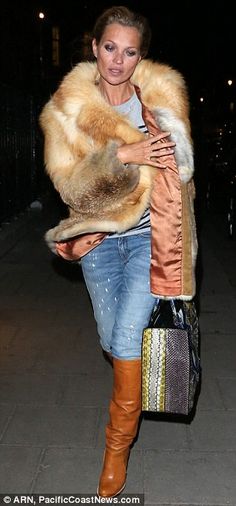 a woman walking down the street carrying a handbag and fur stole around her shoulders