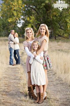 three women and one man are standing on a dirt path in the middle of an open field