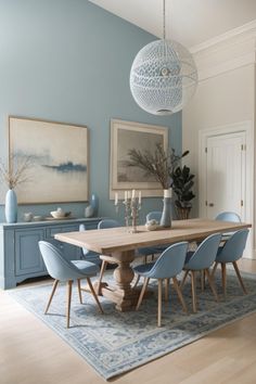 a dining room table with blue chairs and artwork on the wall in front of it