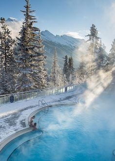 a person sitting in the middle of a blue pool surrounded by snow covered mountains and pine trees