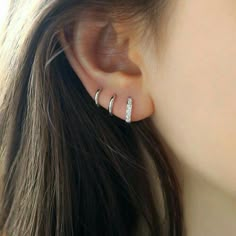 a woman's ear is shown with two small silver hoops on it, and one has a single diamond bar in the middle