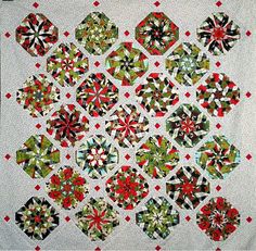 a quilted wall hanging with red and green flowers on the front, along with black and white squares