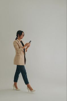 a woman is walking and looking at her cell phone while wearing a blazer jacket