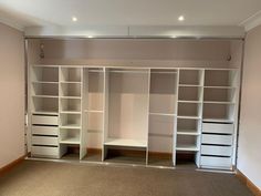 an empty room with several white shelves and drawers on the wall, in front of a beige carpeted floor