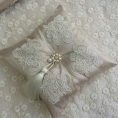 a decorative pillow on a bed with white lace and pearls in the center, along with a beaded brooch