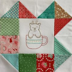 a close up of a patchwork quilt with a bear in a cup on it