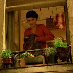 a woman standing in front of a window with potted plants on the windowsill