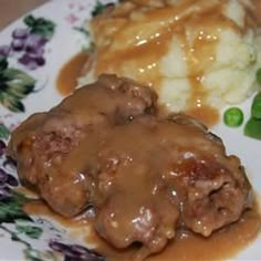 a plate topped with meat and gravy covered in gravy next to green beans