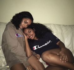 two young women sitting on top of a white couch next to each other and smiling at the camera