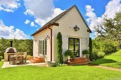 a small white house sitting in the middle of a lush green field next to a picnic table