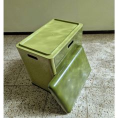 a green trash can sitting on top of a tiled floor