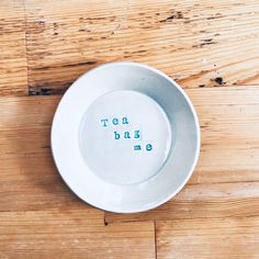 a white plate with the words tea bag me on it sitting on a wooden table