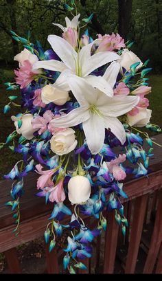 white and blue flowers are hanging from a wooden rail in front of a wooded area