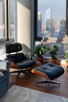 an eames lounge chair and ottoman in front of a window overlooking the city skyline