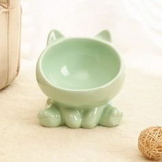 a cat shaped bowl sitting next to a ball of yarn on the floor in front of a bag