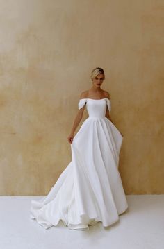 a woman in a white wedding dress standing against a wall with her hands on her hips