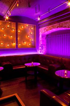 a dimly lit room with leather couches and round tables in front of purple lights