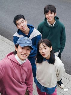 four young people standing next to each other on the sidewalk, looking up at the camera