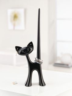 a black cat figurine with rings on it's head and tail, standing next to a candle holder