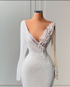 the back of a white dress with long sleeves and sheer lace on it, sitting on a mannequin