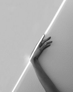 a person's hand on the corner of a wall with white paint and light coming through it