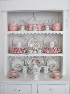 a white china cabinet with dishes and cups on top of it, all decorated in pink