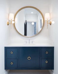 a bathroom vanity with blue drawers and a round mirror on the wall, along with two lamps