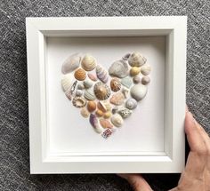 a heart made out of seashells in a white frame on a gray carpet