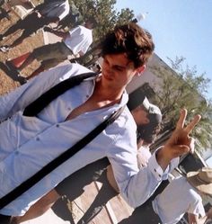 a man in white shirt and black tie making the peace sign with his hand while standing next to other people