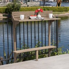 a wooden bench sitting next to a lake filled with flowers and two cups on top of it