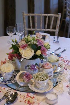 an arrangement of tea cups and saucers on a table with floral centerpieces